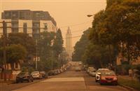 Smoky scene of residential road featuring parked cars some cars driving centred in the image surrounded by trees tall residential building and tall tower