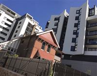 Tilted image with historic red brick building towered over by white contemporary residential buildings on blue sky