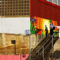 Split image of outdoor stairway with left side untreated sandstone and brick wall divided by directional pole to right side featuring colourful wall graffiti and person walking down stairway