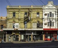 Historic buildings in green and white on main road featuring powerlines one person and shopfronts in white and red one with a sign Fast Food Equipment