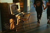 Sunset streetscape with old public piano against yellow building on left with couple walking hand in hand on right