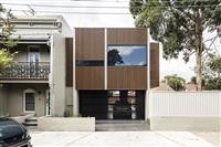 Streetfront image of a contemporary building with wooden slatted frontage small and large rectangular windows and darkened carport below