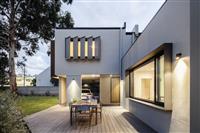 Outdoor setting area with wooden decking white facade with slatted window and door finishings large black framed window with grassed and tree topped backyard area to left