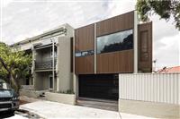 Streetfront image taken from slight angle of a contemporary building with wooden slatted frontage small and large rectangular windows and darkened carport below