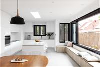 Indoor kitchen and dining area with large black pendant light clean white cabinetry black framed windows wooden dining table front left and bench seating beneath window on right