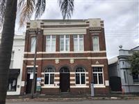 Building exterior streetfrontage of a historic red brick building with creme features a flat facade and white framed large windows