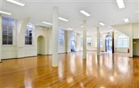 Interior large open hall space with warm wooden floors multiple white columns white rectangular ceiling lights and large windows