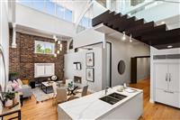 Apartment living and kitchen interior with white walls warm timber floors white marble benchtops exposed brick feature wall and dark wooden steps leading to mezzanine level
