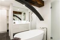 Apartment bathroom interior with white cabinetry bath and tiled walls exposed timber beam and iron support also reflected in mirror cabinets