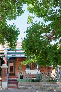 Streetfront of red brick residential home with green features sandstone wall and large tree framing the image