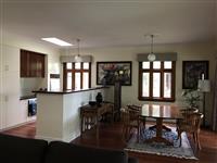 Interior kitchen and dining space with timber floors white walls white and timber cabinets timber framed windows two handing white pendant lights and wooden dining setting