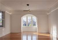 Interior open space with timber floors white walls central window looking out onto residential street plus a single three pronged contemporary light fixture