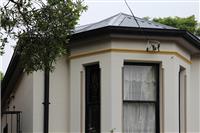 Close up of streetfront exterior featuring creme building with yellow features and grey roof with small natural framing on left