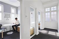 White light filled interior space with multiple panelled windows single figure sitting in a small study room at a white table 