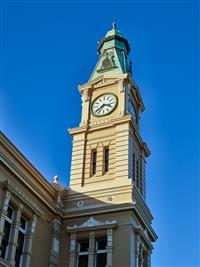 Afternoon scene of yellow and creme clock tower spire with green top surrounded by clear blue sky