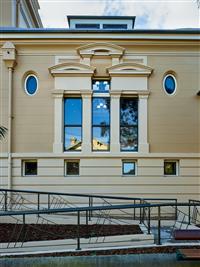 Yellow and creme building exterior showing various windows of circular rectangular and square shapes plus winding ramp featured in foreground