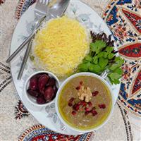Persian stew, brown sauce in bowl accompanied by serving spoon with decorative table cloth and bowl of dates
