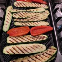 Grilled vegetables zuchinni and capsicums sit on grilling iron with grill marks