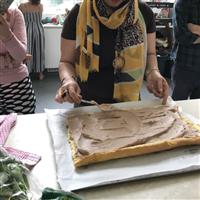 Elham makes rolette Persian sweet, rectangular sponge has chocolate cream spread on centre, arms and hands in shot