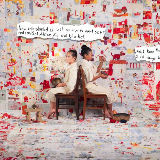 Two children sit on wooden chairs facing away from each other in a colourful patchowrk coloured room
