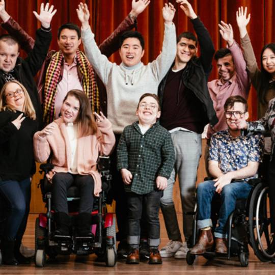 People of varying abilities posing for a picture smiling with their hands in the air