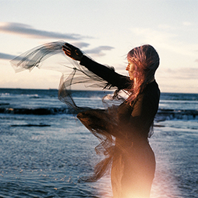 A woman with long hair and a scarf that is blowing in the wind on the beach