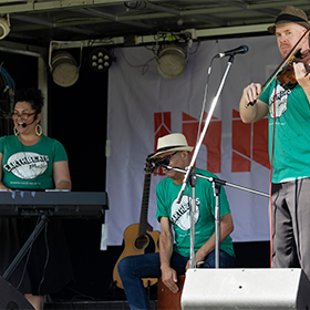 three musicians wearing green tops play on stage