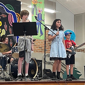 Students on stage playing in front of a colourful backdrop