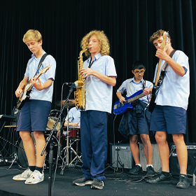 Four students in white tops and blue shorts play instruments