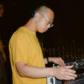 Side shot of a DJ in a yellow tshirt and headphones on arching over DJ decks
