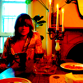 A man with long hair sits at the kitchen table bathed in red light