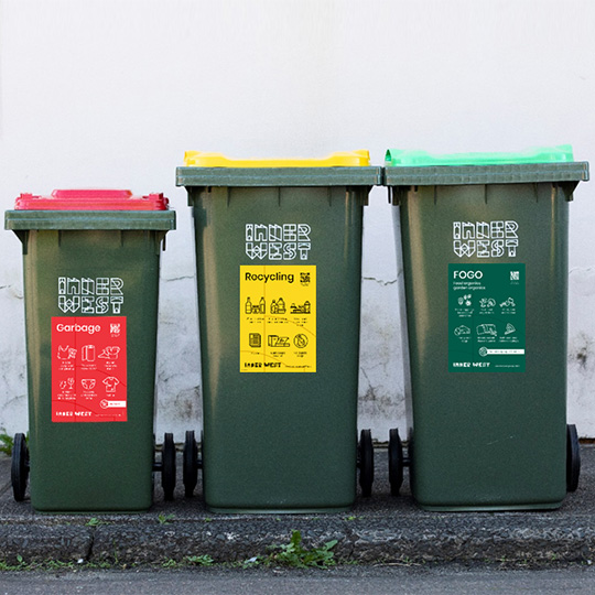 Three bins arranged on a kerbside (red lid and yellow lid and green lid)