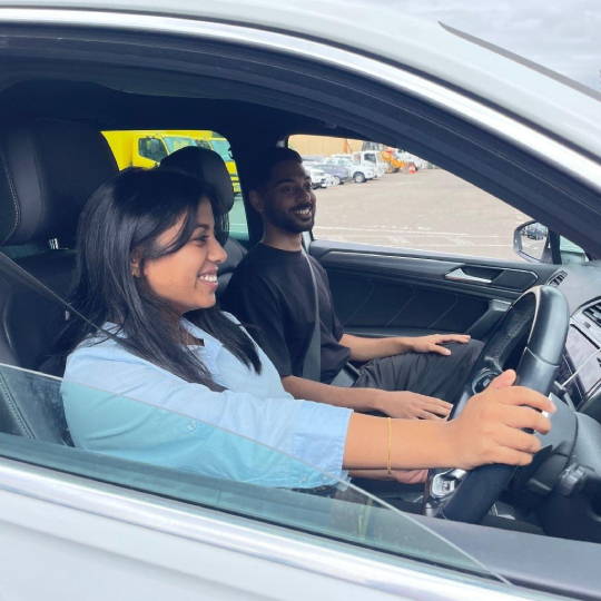 A man and woman smile driving a silver car