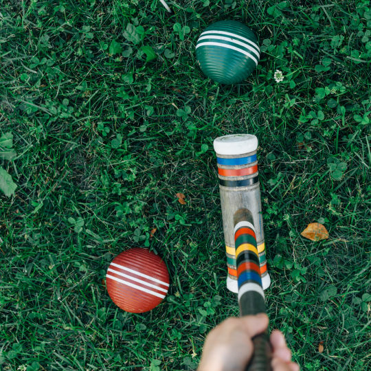Croquet club held in front of a green ball ready to hit and a red ball to the left of the club