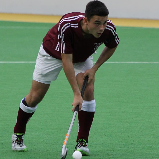 Male player in maroon uniform with ball and hockey stick