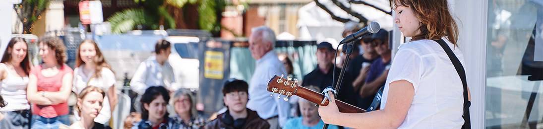 A woman plays guitar to a crowd on the street