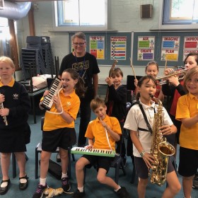 A group of eight students with their teacher all holding a variety of musical instruments in a classroom setting