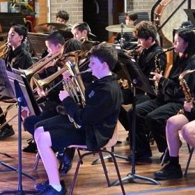 A large group of students all sitting playing a variety of brass instruments