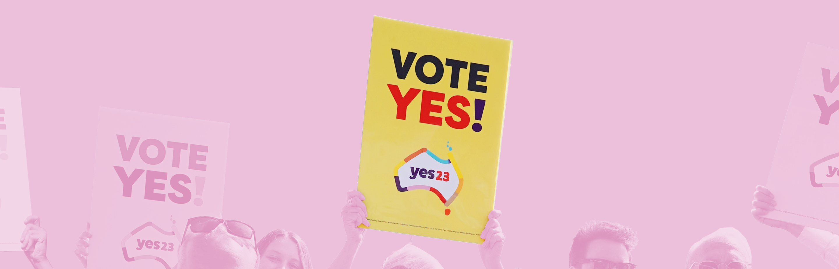 A pink tinted rectangular banner showing a group of people holding Yes banners; a bright yellow banner in the centre reads Yes 23 in red letters.