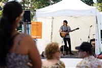 A solo guitarist plays underneath a white marquee with audience members framing the foreground