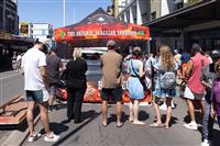 Marrickville streetscape of people lining up for food from a branded marquee with text 