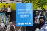 A blue sign explaining the Sensory Space with people seen in the background enjoying the space