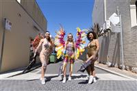 An open laneway with three people posing in the foreground wearing brightly coloured Brazilian dancing outfits with lots of feathers and glitter