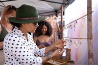 A close image of a person wearing a green hat and black and white spotted shirt inspecting delicate handmade jewellery