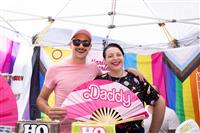 A photo bursting with rainbow colours featuring two happy people holding a large pink fan with the text 