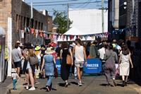 A Marrickville laneway packed with people enjoying a band performance, seen under a marquee at the very end. The laneway is decorated with colourful bunting.