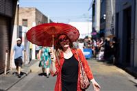 A happy person holding a red fabric umbrella and a red jacket over a black shirt with a busy laneway seen in the background