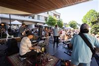 A back corner of stage shot of a band including a drummer, two guitarists and a trumpet playing to a large audience