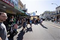 A wide streetscape of people dancing to music played from a small white marquee with pink bunting, and a DJ seen playing inside