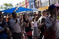 A close shot of a crowd of people gathered on a streetscape cheering a stage performance behind the photographer